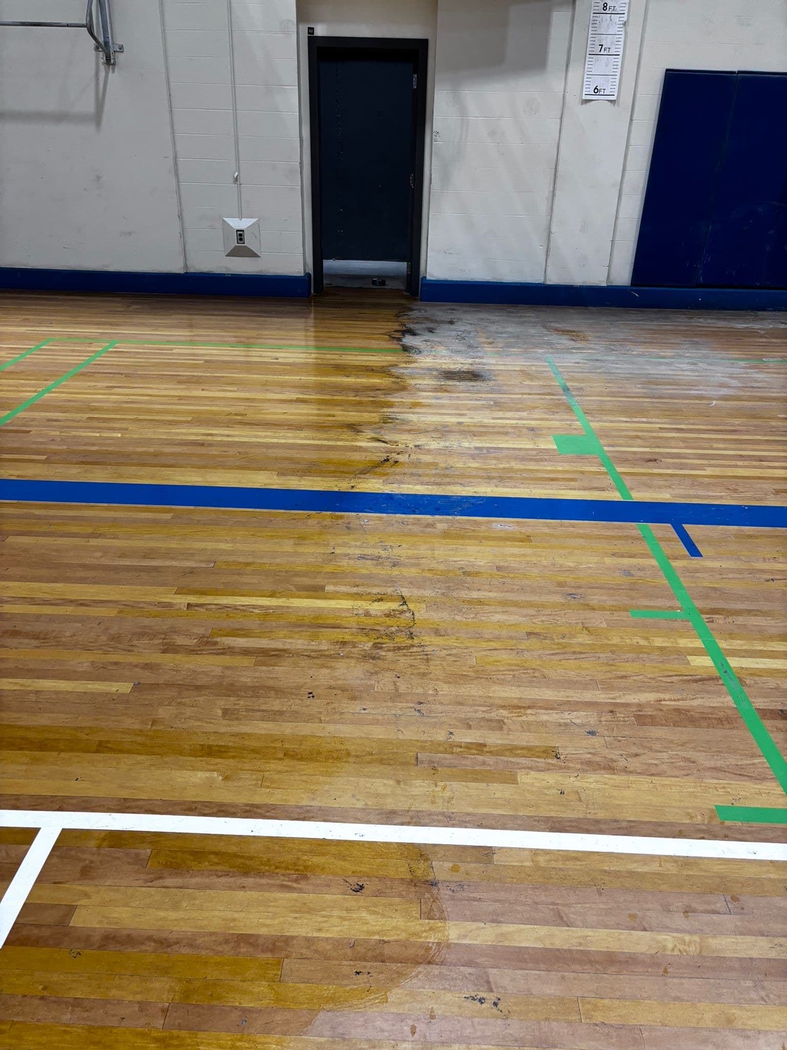 Gym floor during cleaning, with a golden cleaned section on the left beside the duller, untouched section on the right.