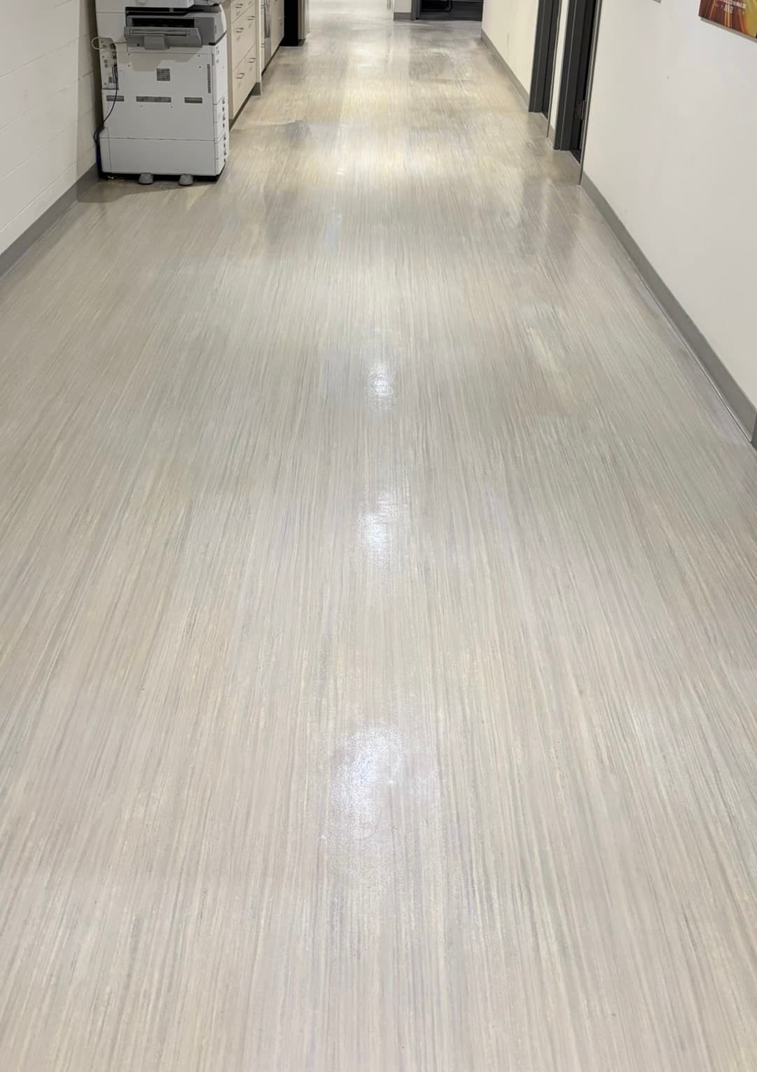 Cleaned commercial hallway floor with a reflective finish beside office doorways and a copier.